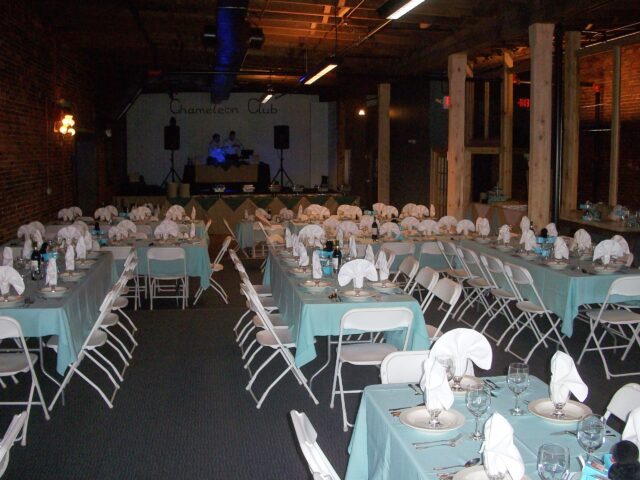 Tables with light blue tablecloths and a stage with sound system are arranged for a birthday party at Chameleon.