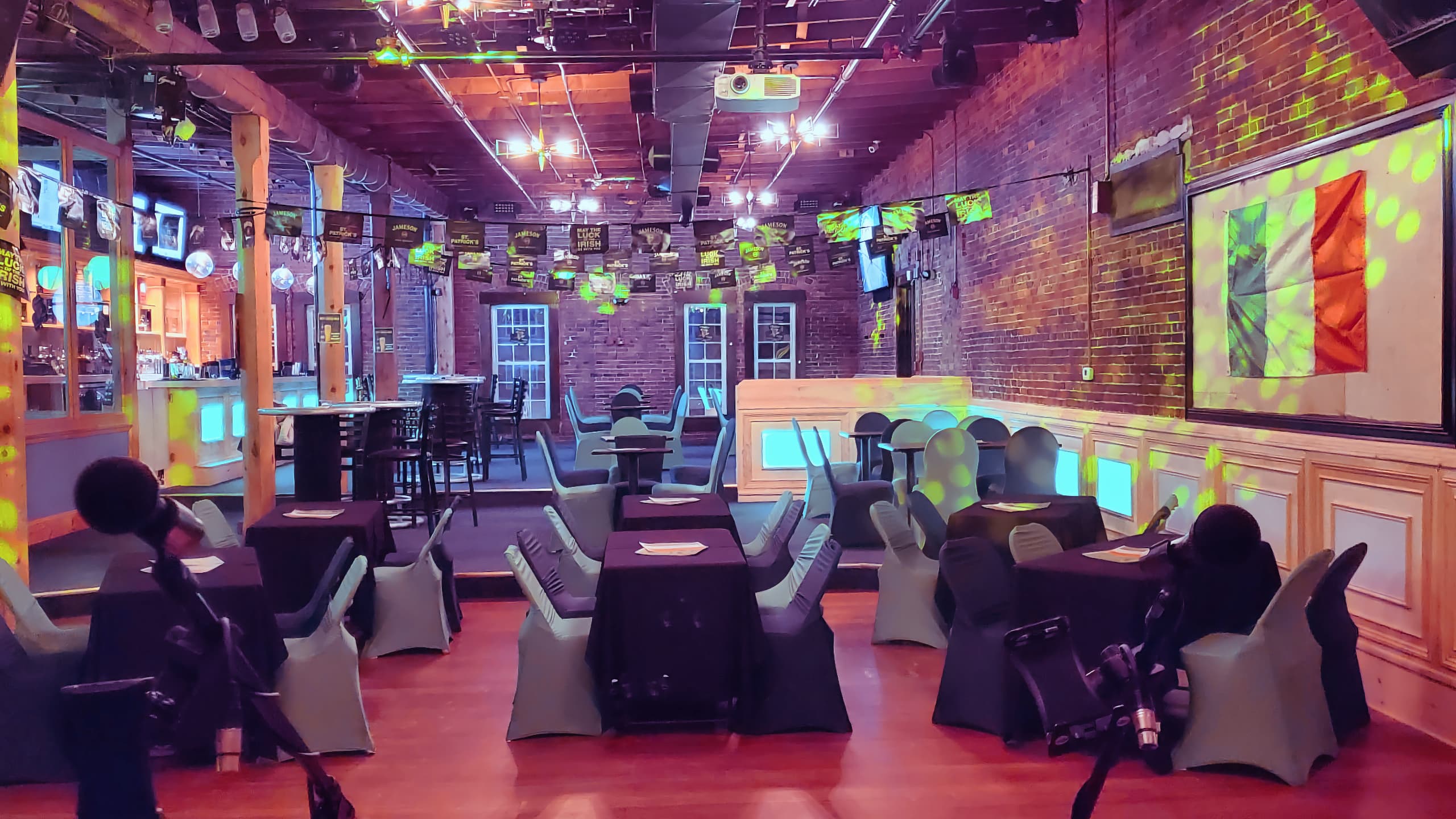 Black tables with alternating black and green chairs are lit by green lights. The Flag or Ireland is mounted on the wall for St. Patrick's Day at Chameleon.