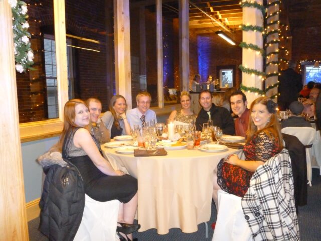 A table of wedding guests are seated and smiling during a wedding at Chameleon.