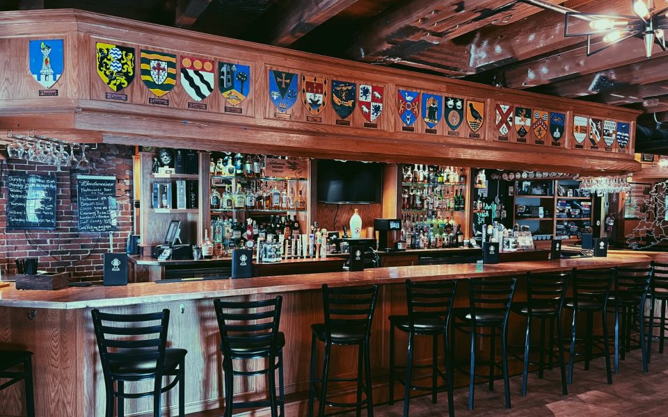 The Cara Irish Pub bar area with stocked shelves, ample seating, and the flags over Ireland hung above the bar.