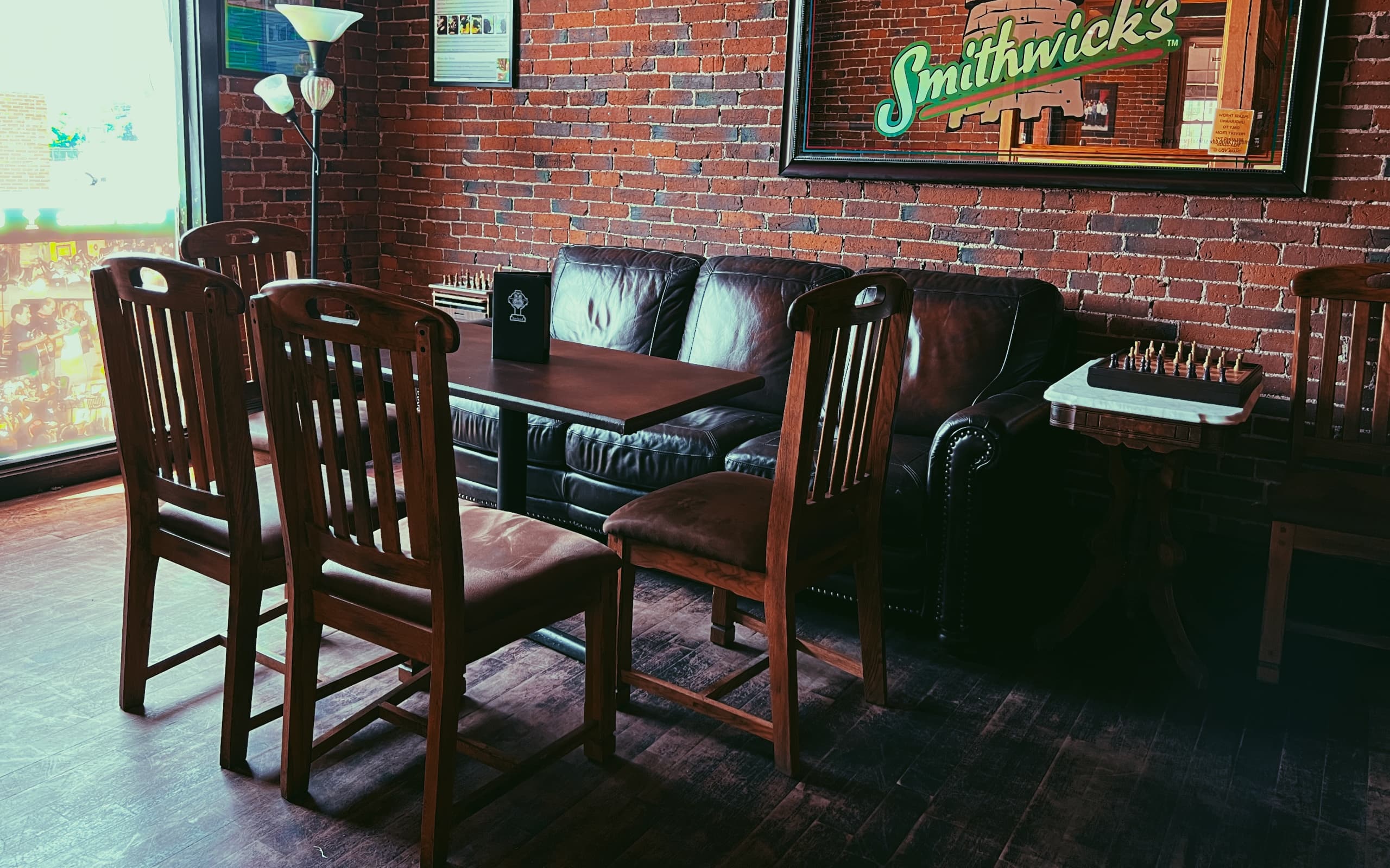 Seating area at Cara Irish Pub. A table and a comfortable couch is shown with artwork on the historic brick walls and a game of chess at the table.